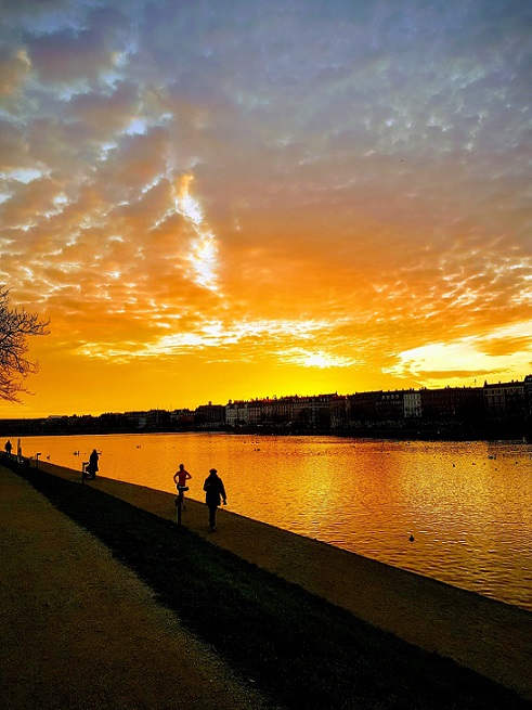 A sunset over a Scandanavian river, with people's silhouettes in the foregrounde